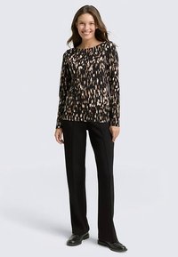 Svart långärmad skjorta med ett beige abstrakt mönster, kombinerad med skräddarsydda svarta byxor och svarta skor. Slätt, lätt tyg.