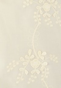 Tessuto bianco con ricami intricati che presentano motivi floreali e linee curve, evidenziando la texture e i dettagli sottili in filo bianco sporco.