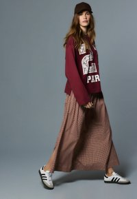 Vaarikapunane dressipluus valge kirjaga, pikk ruuduline pruun seelik ja must-valged spordijalatsid. Aksessuaaride hulgas on pruun nokamüts.