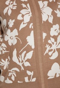 Cardigan tricotat floral în nuanțe de piersică, cu modele de flori albe, țesătură texturată și un detaliu central cu nervuri care se desfășoară vertical.
