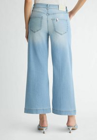 Jean large bleu clair avec taille haute, dotée de deux poches arrière et d'une étiquette en cuir au niveau de la ceinture.