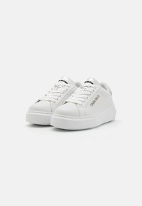 White leather sneakers with a textured surface, round toe, flat platform sole, and silver accents, featuring prominent black logo on tongue.