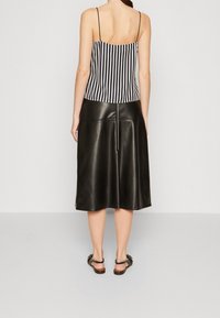 Schwarzer Leder-Midirock mit glatter Textur, kombiniert mit einem schwarz-weiß gestreiften Camisole mit dünnen Trägern, von hinten betrachtet.
