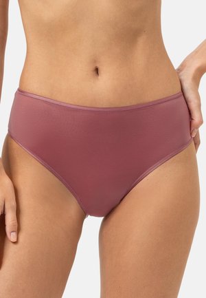 Femme portant un sous-vêtement taille haute mauve, une main posée sur la hanche et l'autre détendue le long du corps.