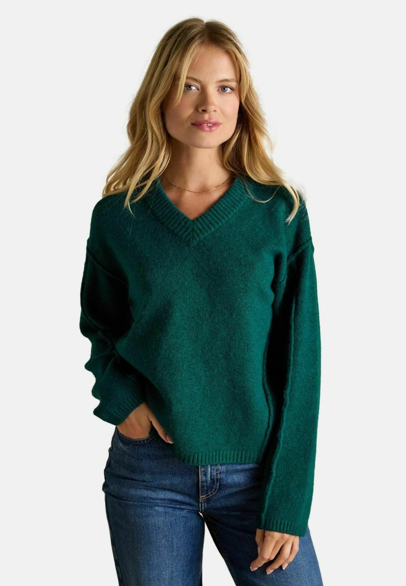 Pulover teal cu decolteu în formă de V, realizat dintr-un material moale și texturat, cu o croială lejeră și manșete cu nervuri, asortat cu blugi din denim albastru.