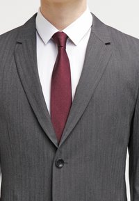 Grau gestreifter Blazer mit Reverskragen, Ein-Knopf-Verschluss, getragen über einem weißen Hemd und einer strukturierten burgunderroten Krawatte.