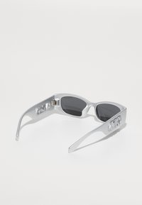 Ochelari de soare argintii cu lentile ovale, un design elegant, decupaje detaliate pe brate și lentile întunecate.