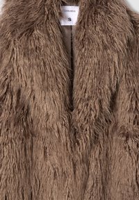 Cappotto in pelliccia sintetica marrone e pelosa con una lunga texture shaggy. Presenta una chiusura a gancio singolo e un'etichetta interna che indica la taglia S.