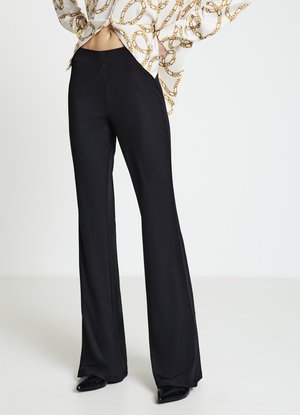 Pantaloni neri a zampa in tessuto liscio con vita aderente. Presentano un design pulito e una leggera lucentezza, abbinati a calzature nere con punta affilata.