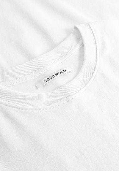 Κοντινή λήψη ενός άσπρου T-shirt με στρογγυλή λαιμόκοψη που δείχνει το ραμμένο γιακά και μια ετικέτα της μάρκας "WOOD WOOD" στο εσωτερικό του λαιμού.