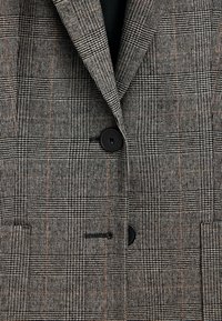 Blazer a quadri grigio e nero con sottili accenti arancioni, dotato di rever a incavo, due bottoni e tasche funzionali. Tessuto strutturato.