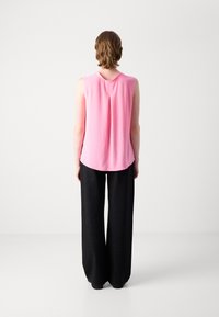 Roze mouwloze top met een ronde halslijn en een plooi aan de achterkant, gecombineerd met losse zwarte broek met subtiele metallic stippen.