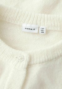 Col roulé en tricot blanc avec un petit bouton décoratif et une étiquette de vêtement indiquant le nom de la marque et la taille 7-8 ans.