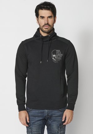 Sudadera negra con alto cuello, mangas texturizadas y un gráfico de calavera en la parte frontal. Cuenta con cordones y un bolsillo tipo canguro.
