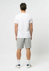 Vyrų baltas medvilninis T-shirt su trumpomis rankovėmis, derinamas su pilkais medvilniniais šortais, matoma iš nugaros. Išvaizdą užbaigia baltos kojinės ir laisvalaikio bateliai.