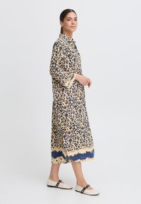 Leopardenmuster Hemdkleid in Beige- und Blautönen, mit langen Ärmeln, Knopfverschluss und einem Saum mit einem blauen Wellenmuster.