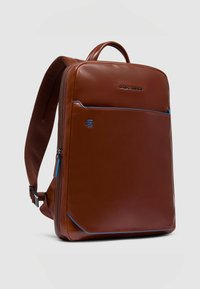 Mochila de cuero marrón con un diseño rectangular elegante, detalles en azul, bolsillo frontal con cremallera y una correa texturizada para mayor comodidad.