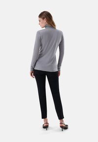 Grauer Rollkragenpullover mit langen Ärmeln, weicher Textur, kombiniert mit schwarzen, maßgeschneiderten Hosen, slim fit, und schwarzen, hohen Sandalen.