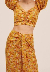 Ensemble deux pièces composé d'un haut court et d'une jupe en tissu jaune avec des motifs floraux. Le haut présente des manches bouffantes et un design ajusté.