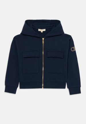 Sweat à capuche zippé bleu marine avec poches avant à rabat, manches longues et un logo discret sur la manche gauche.