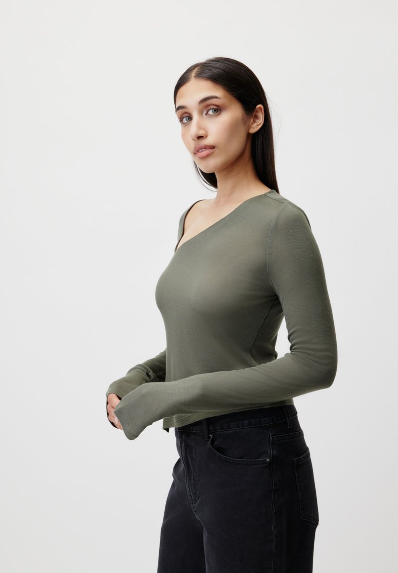 Top a maniche lunghe di colore verde oliva con scollo diagonale e silhouette aderente. Tessuto morbido e maniche e orlo allungati per una vestibilità rilassata.