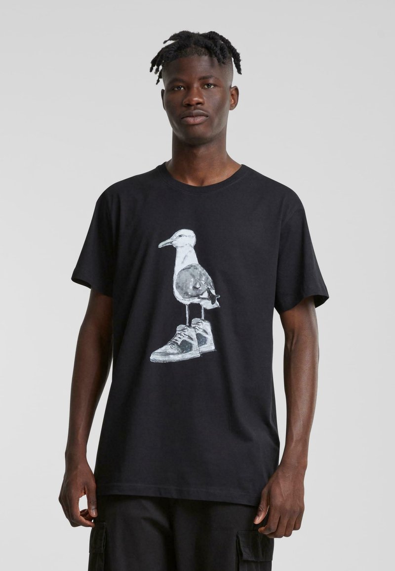Sort kortærmet t-shirt med et grafisk motiv af en fugl iført sneakers, med en enkel, glat tekstur og afslappet pasform.