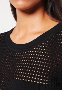 Schwarzer Strickpullover mit strukturiertem, offenem Netzdesign. Verfügt über einen runden Halsausschnitt und gerippte Akzente an Kragen und Saum.