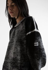 Μαύρος και γκρί πουλόβερ με σχέδιο και υφή, με ριγέ κολάρο. Διαθέτει μια λευκή διακοσμητική γραμμή και ετικέτα λογότυπου στο μανίκι.