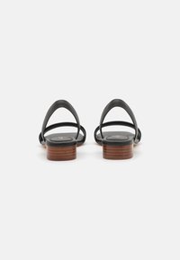 Sandali in pelle nera con un design minimalista, caratterizzati da sottili cinturini e un tacco a blocco in legno. Texture liscia e forma arrotondata.