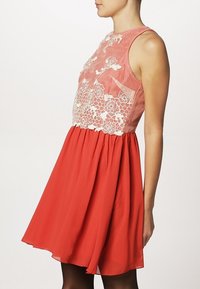 Červené šaty s přiléhavým korzetem, který má květinovou krajku, a rozšířenou sukní. Materiál je hladký a lehký.