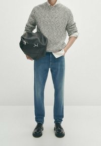 Pull en maille texturée grise superposé à une chemise blanche à col, associé à un jean droit bleu clair et des chaussures noires à lacets. Sac noir tenu à la main.