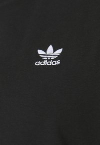 T-shirt in cotone nero con logo Adidas ricamato bianco e design a tre foglie nella zona sinistra del petto. Texture liscia.