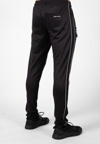 Zwarte sportbroek met witte zijstrepen, voorzien van een achterzak en een ritszak aan de zijkant, gemaakt van glad, rekbaar materiaal.