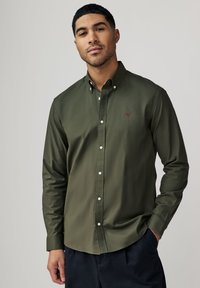 Olijf groene overhemd met knopen en een kraag, voorzien van witte knopen en een klein logo op de borst. Zacht stof met een gladde textuur.