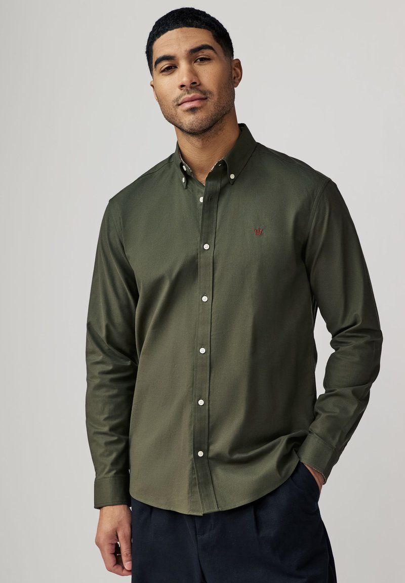 Olijf groene overhemd met knopen en een kraag, voorzien van witte knopen en een klein logo op de borst. Zacht stof met een gladde textuur.