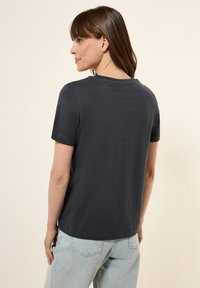 Mörkgrå t-shirt med kort ärm och rund halsringning, enkel design och en lätt struktur. Har en liten logotypdetalj nära kragen.