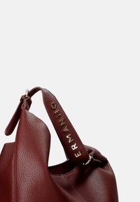 Borsa a tracolla in pelle rossa con finitura testurizzata. Presenta un logo dorato prominente su una tracolla piatta e un design morbido e sformato.