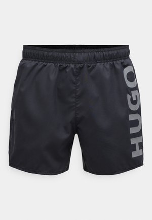 Black swim shorts with an elastic waist, featuring a smooth texture and a large grey logo on the side.