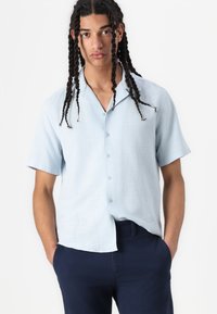Chemise bleu clair à manches courtes avec col, en tissu texturé et à motif à carreaux subtil, associée à un pantalon bleu marine.
