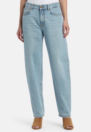 Világoskék, magasderekú, egyenes szárú farmer, barna, nyitott orrú, sarokkal ellátott cipőkkel viselve, álló emberen.