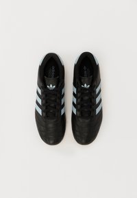 Melni ādas sporta apavi ar gaiši zilām svītrām, noapaļots purngalis un teksturēta virsma. Aprīkoti ar melniem šņorēm un Adidas logo uz mēles.