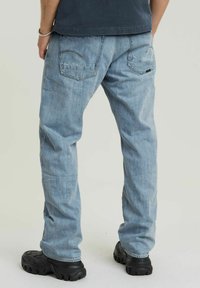 Jeans din denim de culoare bleu deschis, cu croială dreaptă, având două buzunare la spate și un efect ușor de spălare. Asortați cu pantofi din cauciuc negri.