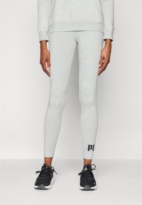 Leggings en coton gris clair au design ajusté, ornés d'un logo noir sur le bas de la jambe. Associés à des chaussures de sport noires.