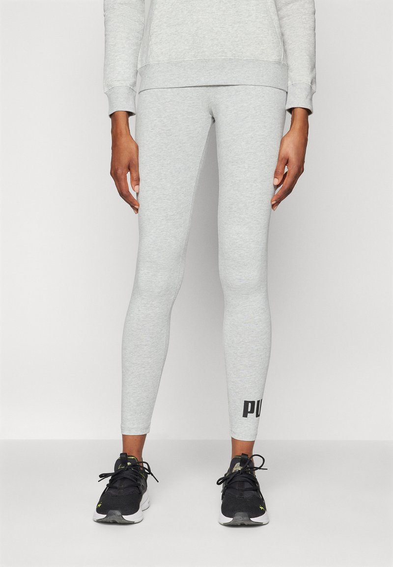 Leggings en coton gris clair au design ajusté, ornés d'un logo noir sur le bas de la jambe. Associés à des chaussures de sport noires.