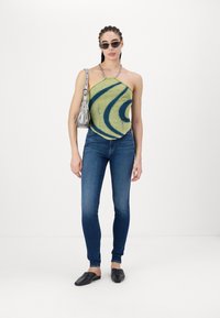 Green halter top with blue swirl pattern, blue skinny jeans, black slip-on shoes, and silver bag with chain strap.