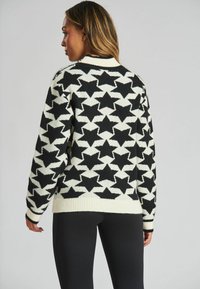 Maglione bianco e nero con motivo a stelle, polsini e orlo a coste, con una texture in maglia comoda e una vestibilità rilassata.