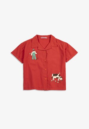 Červená košeľa s krátkym rukávom na gombíky s golierom, na ktorej je ilustrácia farmára držiaceho vidly a kravy so strakatým čiernym a bielym sfarbením, ktorá sa pasie.