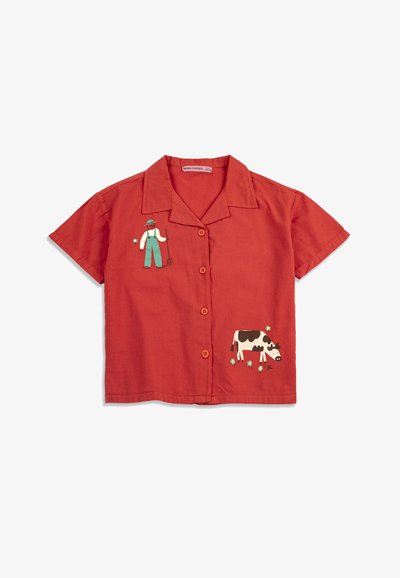 Chemise rouge à manches courtes avec col et boutons, ornée d'une illustration d'un fermier tenant une fourche et d'une vache en noir et blanc pâturant.