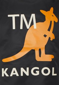 Fundo preto com um gráfico de canguru laranja em destaque e texto branco a ler "TM KANGOL" em baixo. Textura suave e cores vibrantes.