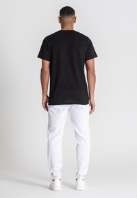 Czarny prążkowany t-shirt z krótkim rękawem, prostym dołem i okrągłym dekoltem, w połączeniu z białymi spodniami i białymi trampkami.